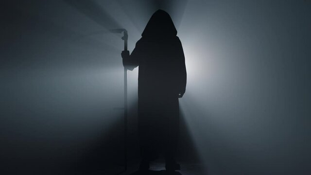 Silhouette grim reaper standing indoors. Death with scythe spotlight background.