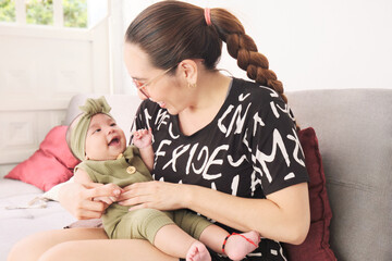 Mamá latina sonríe mientras mira y juega con su bebe, bebe sonríe alegre mientras ve a su mamá