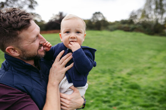 Playful Young Dad Enjoying Baby Boy In Grassy Field.