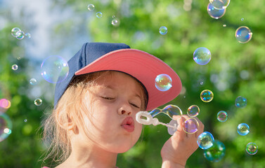 Little girl blows soap bubbles outdoor.