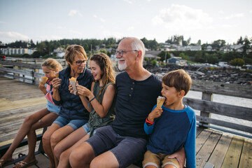 Grandparents and grandkids laugh and sit on a bench on a dock wh