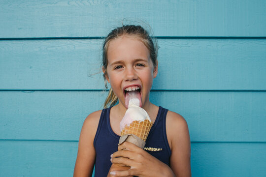 Child licks and enjoys an ice cream cone against a bright wall 