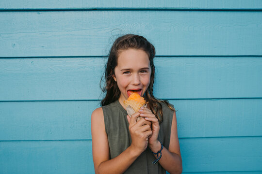 Child licks and enjoys an ice cream cone against a bright wall 