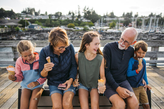 Grandparents and grandkids laugh and sit on a bench on a dock wh