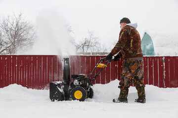 Senior male removing snow near barrier
