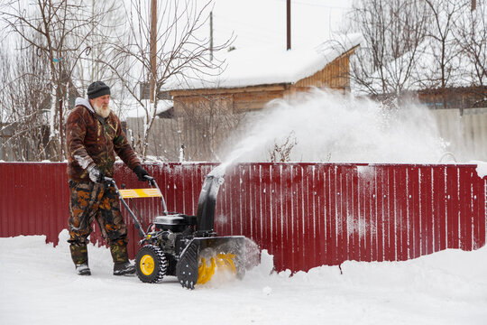 Bearded aged man with machine throwing snow over fence