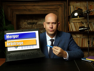 A handsome businessman showing a laptopwith sign Merger Arbitrage .