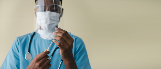 African–American doctor wearing a mask and face shield. Holding a syringe with a bottle of COVID-19 vaccine protection in a laboratory. Concept of protection against the coronavirus.