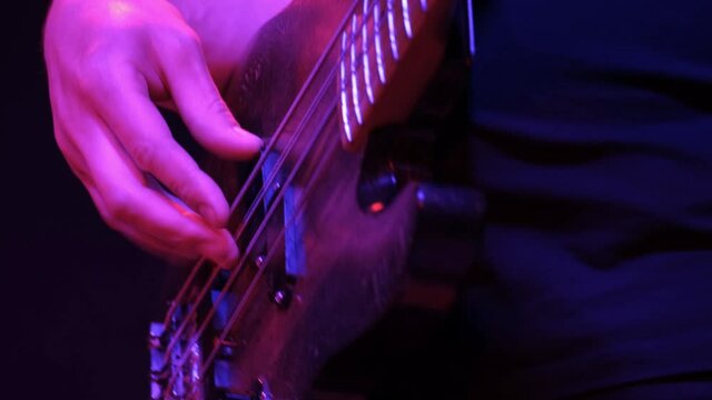 Male guitarist playing electric bass guitar on a rock concert in a club. Red lighting, hands closeup.