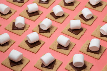 White marshmallow, chocolate bars and graham crackers on a pink background. Pattern of ingredients for s'mores