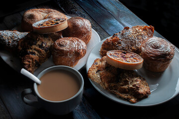 Horizontal sweet bread on a white plate lit by a window in a moody evening morning ambient  with a cup of coffee and cream and a spoon in it dark food, low key light photography baroque renaissance 