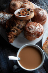 vertical sweet bread on a white plate lit by a window in a moody evening morning ambient  with a cup of coffee and cream and a spoon in it dark food, low key light photography baroque renaissance 