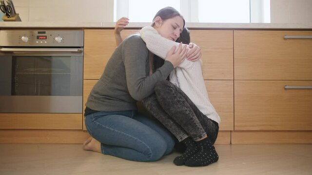 Upset teenage girl hugging and embracing her mother sitting on kitchen floor. Mental problems and depression of teens