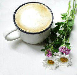 Cup of fresh coffee with milk foam and wild flowers on white background, top view