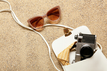Stylish sunglasses with bag and photo camera on sand