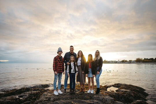 Casual, Backlit Family Portrait On Rocky Beach At Sunset.