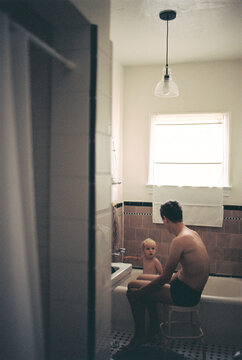 Underexposed film image of toddler taking a bath with help of his father