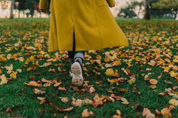 Detail of senior woman from back walking at park with yellow coat in autumn