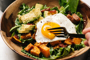 Cutting into an egg over a breakfast salad