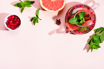 Immunity boosting drink. Mint Tea with cranberries, grapefruit and spices in glass teapot on pink table, trendy shadows