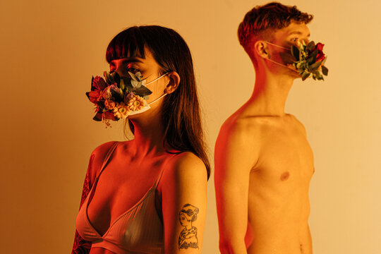 Couple in flower masks standing on beige background