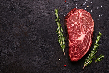 Fresh raw marbled beef rib eye steak and spices on black stone background, copy space