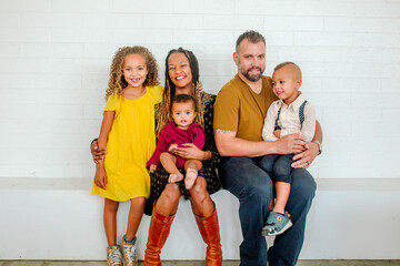 Happy biracial family seated on ledge in front of white wall