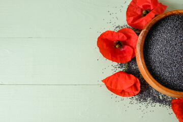 Bowl with poppy seeds and flowers on color wooden background