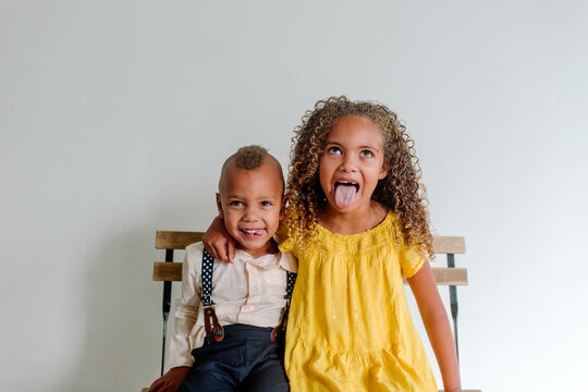 Silly biracial brother and sister sitting next to each sticking out tongues