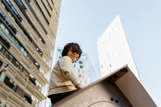 young boy sitting on tiny house roof in city playground against office buildings
