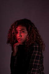 vertical portrait of a young latin woman posing with red ligth and dark background