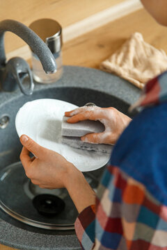 Crop woman washing dishes with detergent