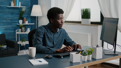 Obraz na płótnie Canvas Authentic black man computer user working from home in cozy flat, remote african american worker typing on computer, freelancer using internet from home office. Online communication, lifestyle and