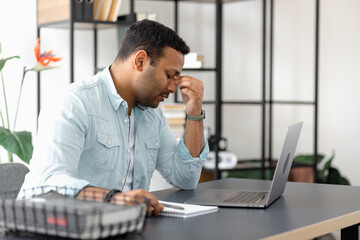 Tired Indian businessman having headache or migraine sitting at the office desk, Young man...