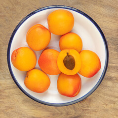 Fresh apricot fruits on white plate over wooden  background. Sweet apricots pile, top view