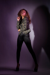vertical portrait of a curly model wearing a jacket, black pants and high heel shoes in a purple backgroung