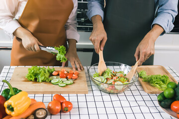 Asian couple enjoying cooking vegetable salad in the kitchen.