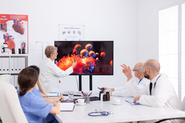 Virolog senior woman discussing about coronavirus symptoms during meeting in conference room. Physician teamwork explaining medical vaccine against global pandemic monitoring virus risk