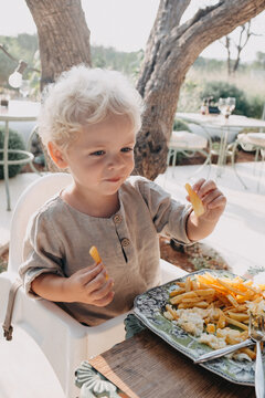 Toddler boy eatting french fries and eggs in a high chair outdoors