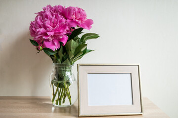 Portrait white picture frame mockup on wooden table. Modern vase with peony. White wall background. Scandinavian interior. 