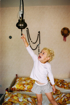 Blond toddler boy on a bed with vintage bedding trying to grap lamp