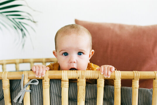Baby girl teething on rattan baby bed