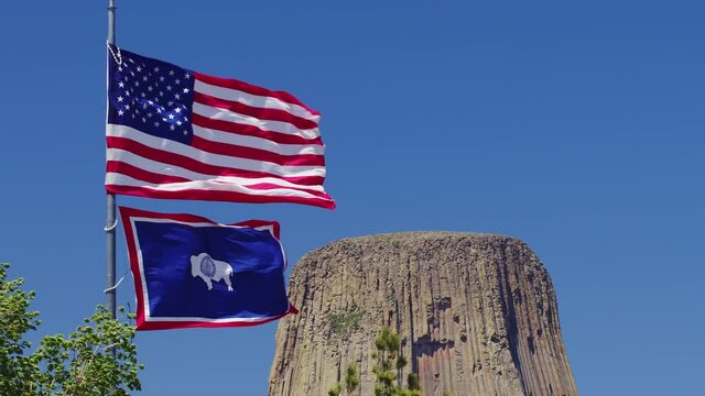 United States of America and Wyoming State flags waving in the wind in front of Devils Tower in Wyoming on sunny day.