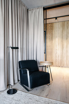 Black armchair in the living room next to brown velvet curtains and a lamp