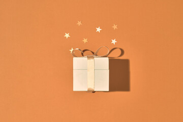Golden gift or present box and stars confetti on color table top view. Flat lay composition for birthday, christmas or wedding.