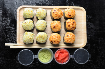 A set of seafood rice rolls wrapped in thin dried sea grass leaves on a wooden platter with ginger and wasabi.