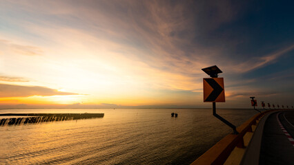 Fototapeta na wymiar View from curve road to sunset skyline over the tropical sea in Thailand. Calm sea with yellow sunset sky. Beauty in nature. Road beside the sea in summer. Summer road trip travel concept. Tranquility