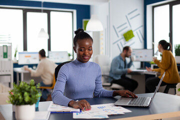 African in marketing corporate office working to finish deadline, checking charts. Diverse team of...
