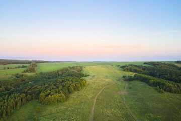 Forested flat terrain with winding dirt roads in the rays of the setting sun. Shooting from a drone.