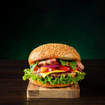 Fresh homemade tasty burger on a wooden cutting board over dark green background. Fast food concept. Copy space.